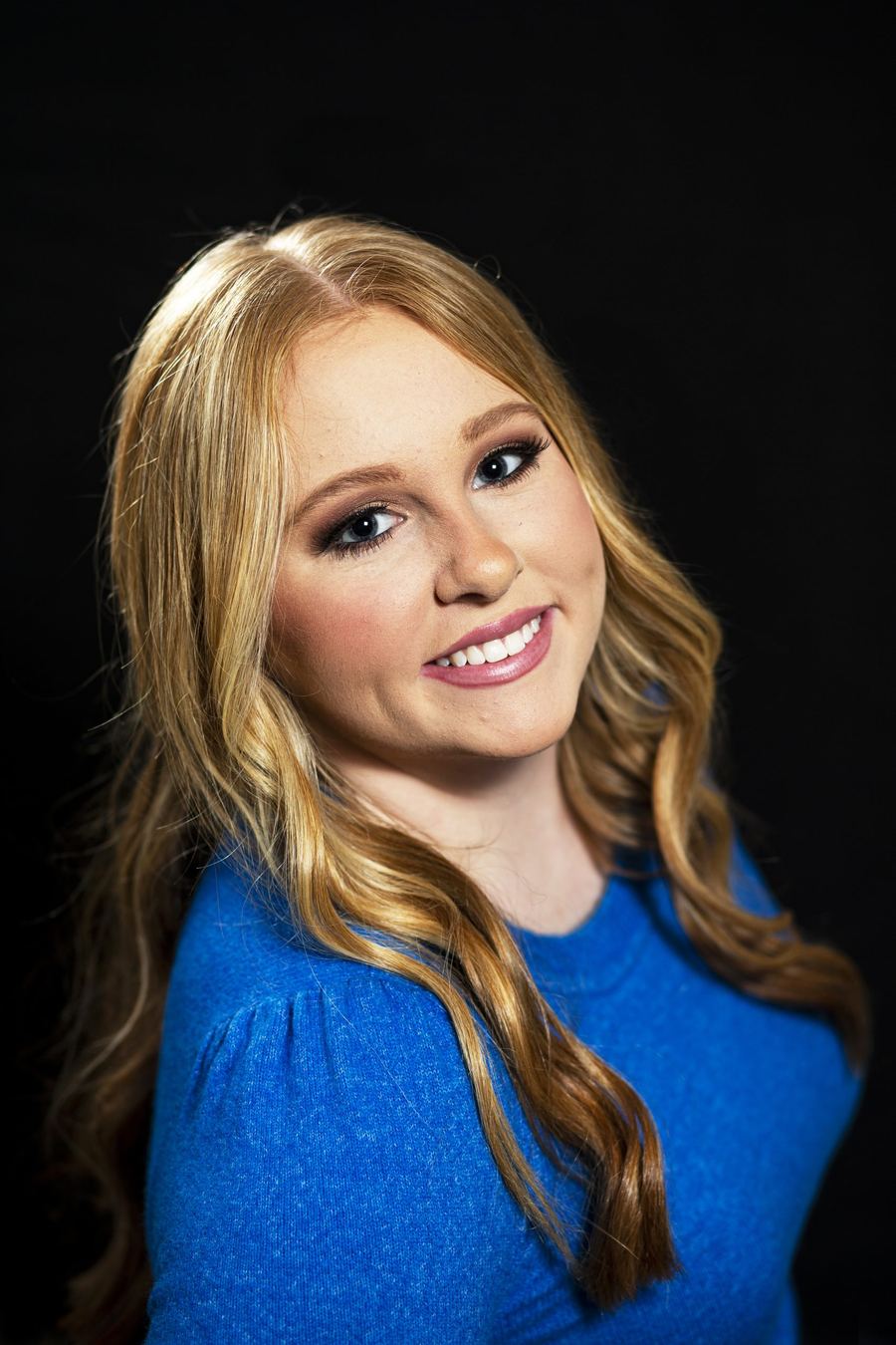 Studio portrait of a young woman in a blue sweater against a black backdrop