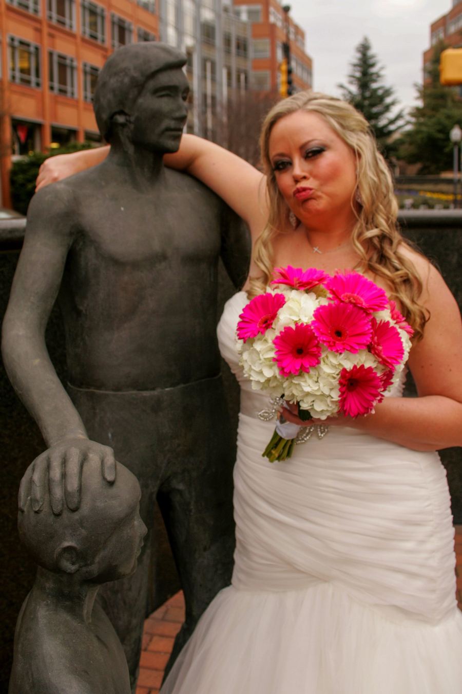 Bride with a pink gerbera bouquet leaning on a bronze statue downtown