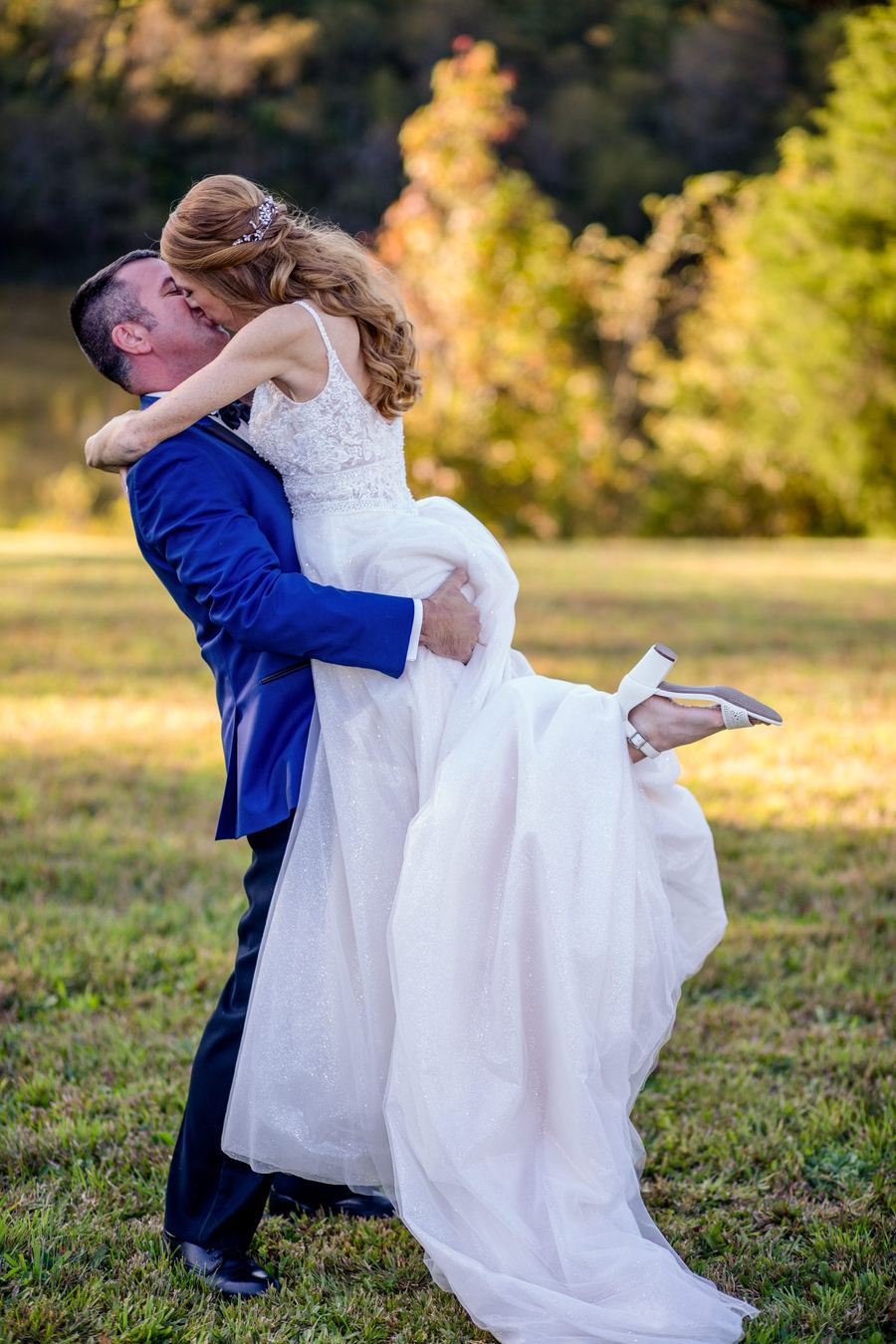 Groom lifting his bride off the ground in an autumn field